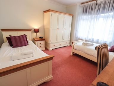 A bedroom with two single beds a wardrobe a bedside table with a lamp and a window with curtains at Gildabrook Cottage in Bowness