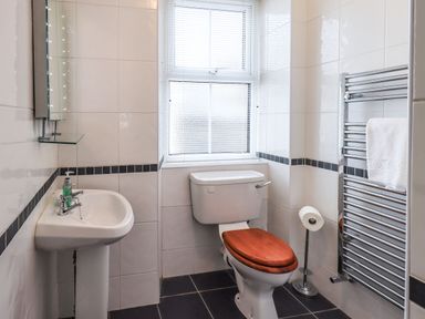 A bathroom with a sink and mirror on the left and a toilet with wooden seat and towel rack on the right at Gildabrook Cottage in Bowness