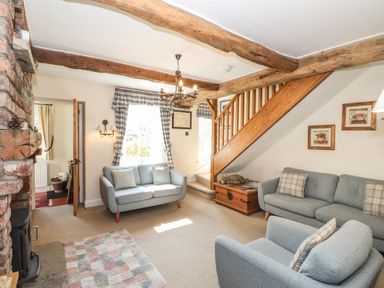 A living room with blue sofas a wooden chest under stairs and exposed wooden beams at Hodge How Cottage in Windermere