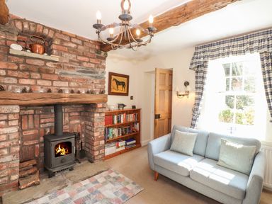 A living room with a brick fireplace wood stove bookshelf and blue sofa at Hodge How Cottage in Windermere