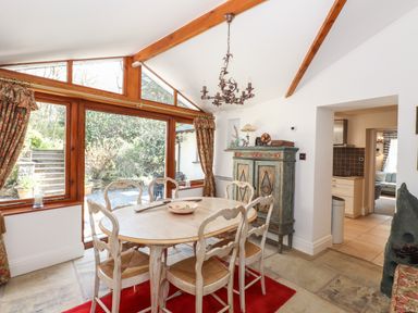 A dining room with wooden table and chairs and large windows overlooking garden at Hodge How Cottage in Windermere