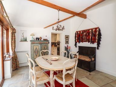A dining room with a round table and six chairs wooden beams on the ceiling and a decorative cabinet at Hodge How Cottage in Windermere