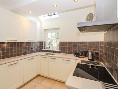 A kitchen with white cabinets brown tiled backsplash and a window at Hodge How Cottage in Windermere
