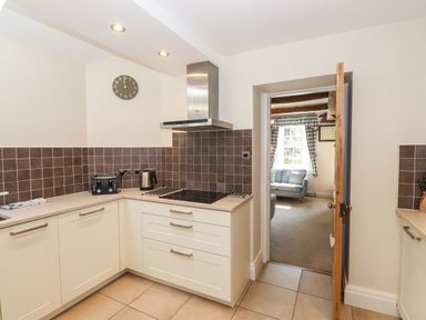 A kitchen with white cabinets brown tiled backsplash a toaster and kettle on the counter and a doorway leading to a living room at Hodge How Cottage in Windermere