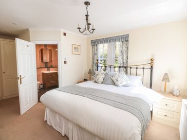 A bedroom with a bed pillows bedside tables a window and an open door leading to a bathroom at Hodge How Cottage in Windermere