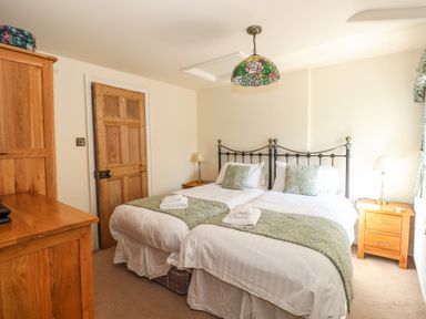 A bedroom with two single beds pushed together wooden furniture and a hanging light at Hodge How Cottage in Windermere