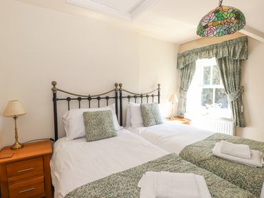 A bedroom with two single beds bedside tables and a window with curtains at Hodge How Cottage in Windermere
