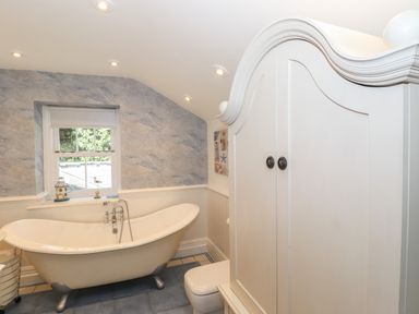 A bathroom with a freestanding bathtub a small window a white cabinet and blue tiled floor at Hodge How Cottage in Windermere