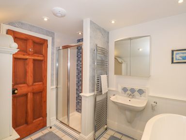 A bathroom with a wooden door shower cubicle towel rail sink and mirror cabinet at Hodge How Cottage in Windermere