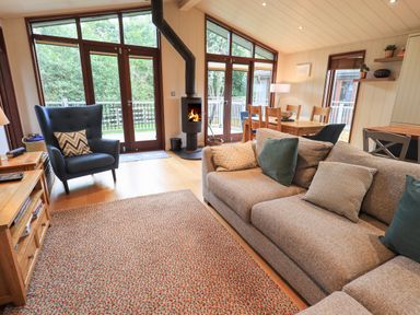 A living room with a sofa pillows armchair wood burning stove dining table and windows at Beck of Beyond in Ambleside