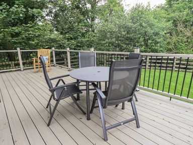 A deck with a round table and four chairs and a wooden rocking chair with a blue cushion at Beck of Beyond in Ambleside