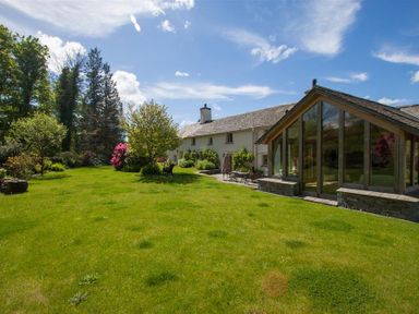 A garden with green grass trees and flowering shrubs outside a house with large glass windows at Old Droomer in Windermere
