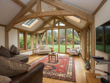 A sitting room with wooden beams large windows armchairs and a patterned red rug at Old Droomer in Windermere