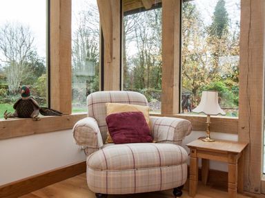 A plaid armchair with cushions next to a wooden side table with a lamp in a room with large windows at Old Droomer in Windermere