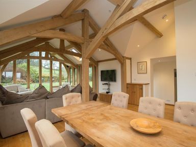 A dining area with a wooden table and beige chairs next to a living room with a sofa and large windows showing a garden at Old Droomer in Windermere