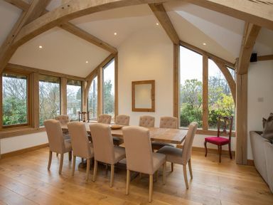 A dining room with a wooden table surrounded by beige chairs and wooden beams at Old Droomer in Windermere