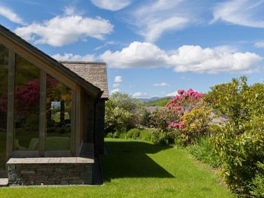 A garden with green grass and flowering bushes next to a building with large windows at Old Droomer Windermere