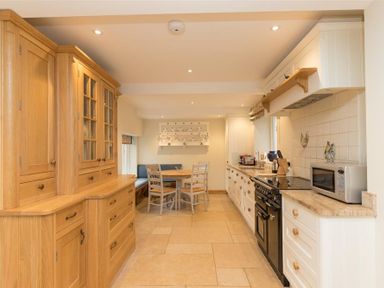 A kitchen with wooden cabinets a dining table with chairs and a black stove at Old Droomer in Windermere