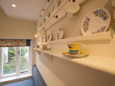 A wall-mounted display shelf with decorative plates and cups near a window and bench seating at Old Droomer in Windermere