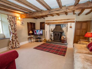 A living room with wooden beams stone fireplace plaid rug and upholstered sofas at Old Droomer in Windermere
