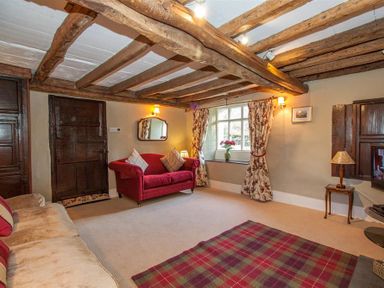 A living room with exposed wooden beams a red sofa and floral curtains at Old Droomer in Windermere
