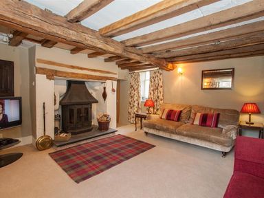 A living room with a fireplace wooden ceiling beams and sofas at Old Droomer in Windermere