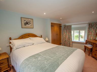 A bedroom with a double bed wooden bedside tables a wooden wardrobe window with floral curtains and a wooden dressing table at Old Droomer in Windermere