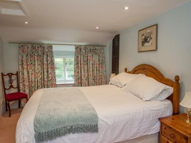 A bedroom with a wooden bed a bedside table with lamp floral curtains and a red chair at Old Droomer in Windermere