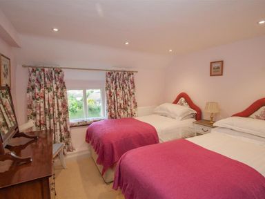 A bedroom with two single beds with pink bedspreads a wooden dresser and floral curtains at Old Droomer in Windermere