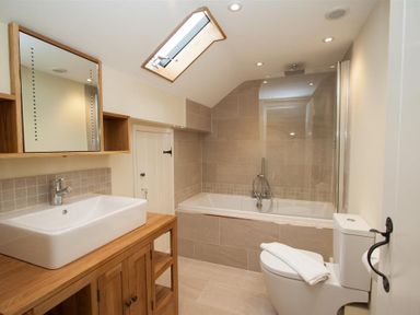 A bathroom with a bathtub a toilet a sink with wooden cabinet and a skylight window at Old Droomer in Windermere