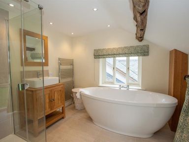 A bathroom with a bathtub a wooden sink cabinet and a glass shower at Old Droomer in Windermere