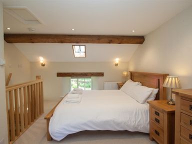 A bedroom with a wooden bed frame white bedding wooden nightstands with lamps and wooden ceiling beams at Old Droomer in Windermere