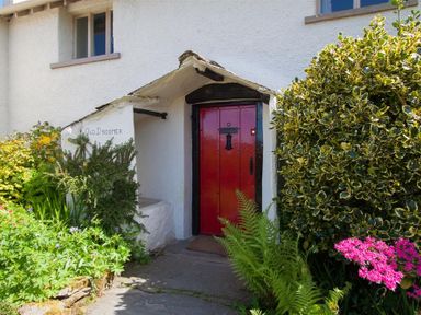 A white house exterior with a small porch and a red door surrounded by green plants and flowers at Old Droomer in Windermere