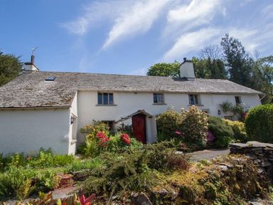 A white cottage with a red door surrounded by flowers and greenery at Old Droomer in Windermere