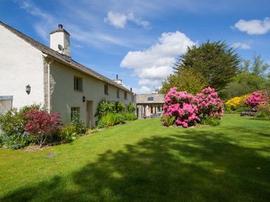 A garden with green grass and flowering bushes next to a white building at Old Droomer in Windermere