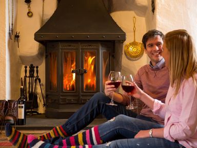 A couple sitting on the floor wearing colorful socks and holding glasses of wine near a fireplace at Old Droomer in Windermere