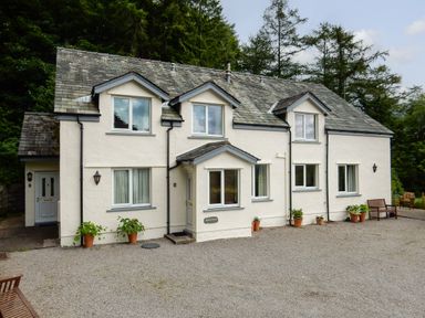 A white two-story house with multiple windows and potted plants on a gravel driveway at Kirkstones in Keswick