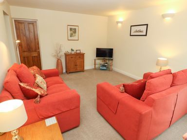 A living room with two red sofas a wooden cabinet a television on a glass stand and wall lights at Kirkstones in Keswick