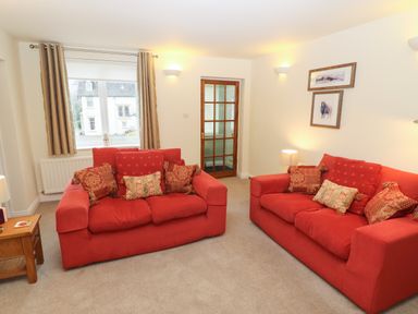 A living room with two red sofas and cushions a wooden side table a window with curtains and a glass door at Kirkstones in Keswick