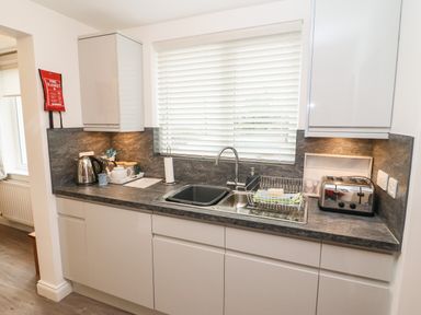 A kitchen countertop with a sink kettle toaster and cabinets under a window with blinds at Kirkstones in Keswick