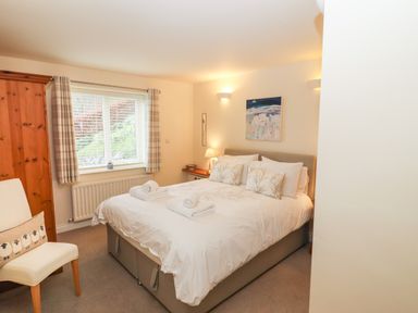 A bedroom with a double bed with pillows and towels bedside table with lamp window with curtains wooden wardrobe and a chair at Kirkstones Keswick