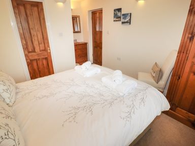 A bedroom with a double bed with rolled towels on it a wooden dresser two wooden doors a white chair with a pillow and two paintings on the wall at Kirkstones in Keswick