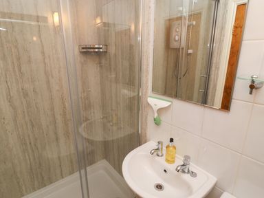 A bathroom with a shower enclosure sink with soap dispenser and a mirror at Kirkstones in Keswick