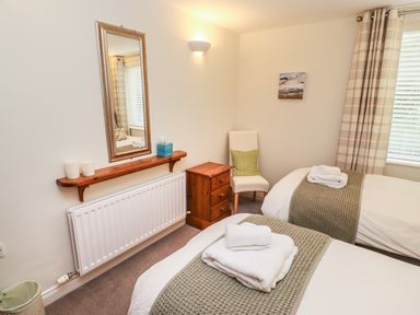 A bedroom with two single beds a wooden nightstand a chair a mirror and a window with plaid curtains at Kirkstones in Keswick