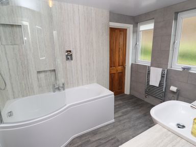 A bathroom with a bathtub shower combination a wooden door two windows a towel rack and a sink at Kirkstones in Keswick