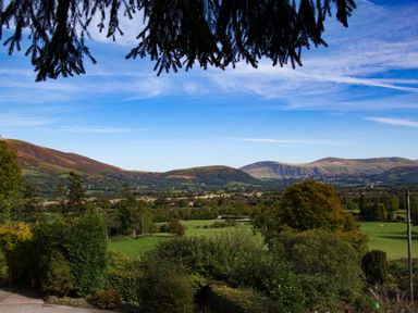 A landscape of green fields trees and hills under a blue sky at Kirkstones in Keswick