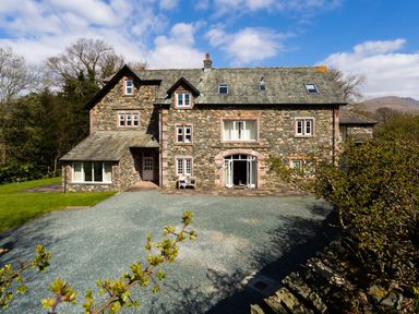 A large stone house with multiple windows and a gravel driveway surrounded by trees at Tethera in Keswick