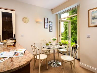 A dining area with a round glass table set for four next to an open door showing greenery outside at Tethera in Keswick