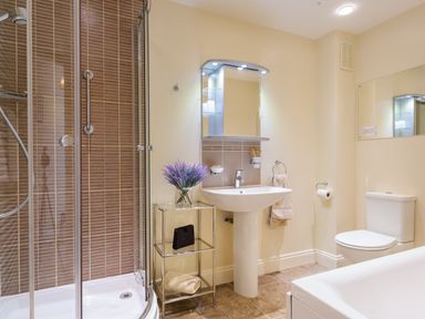 A bathroom with a glass shower enclosure a pedestal sink a toilet and a small metal shelf with a vase of flowers at Tethera in Keswick
