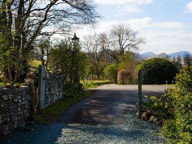 A country road with stone walls trees bushes and mountains in the background at Tethera in Keswick
